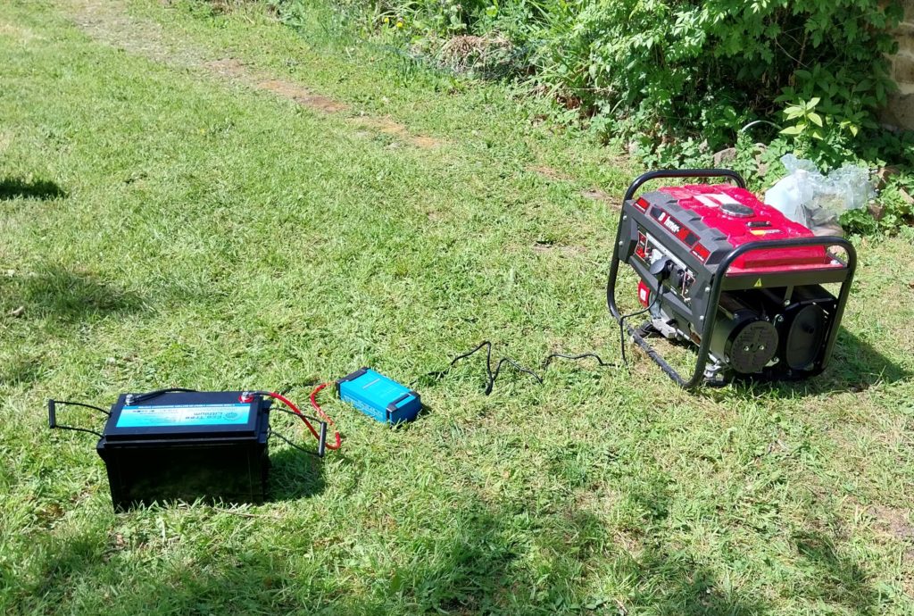 A red generator sits on the grass, connected to a new lithium battery.