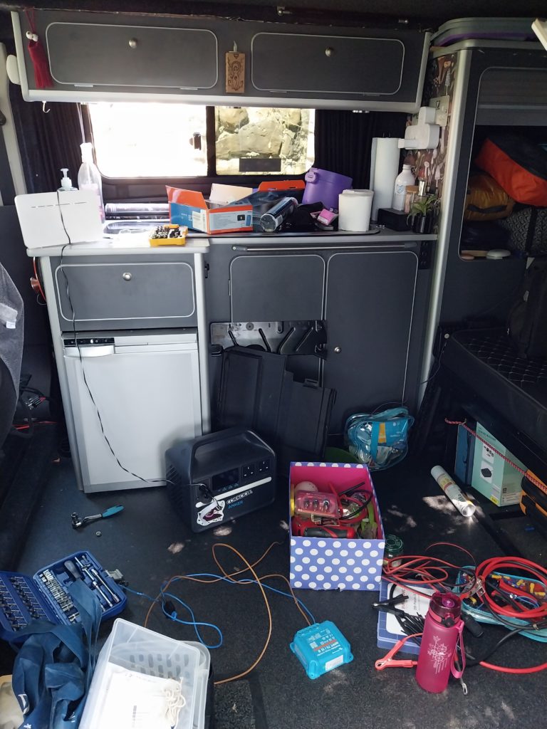 The inside of the campervan, where various cupboard items litter the floor and all available surfaces, having been removed for access.