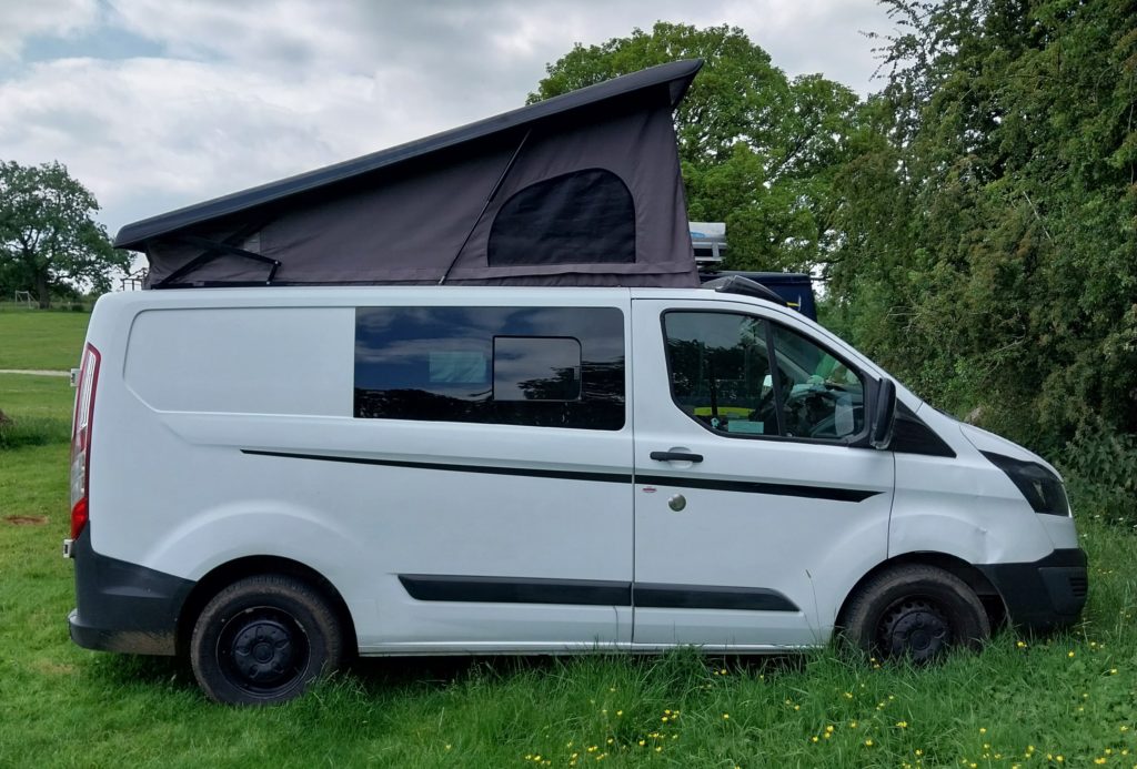 A side view of a white ford transit custom with no more blue stripes.