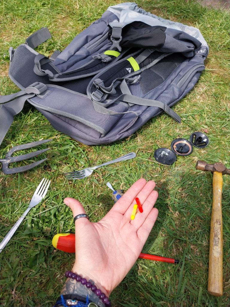 The aftermath of security tag removal. The tools needed and bits of the tag lay in the grass. A hand holds two glass pill shaped capsules of dye, one red and one yellow.
