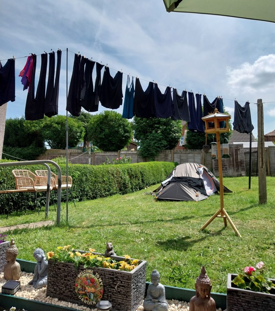 The view from a patio under an umbrella, looking out at a full washing line and a tent.