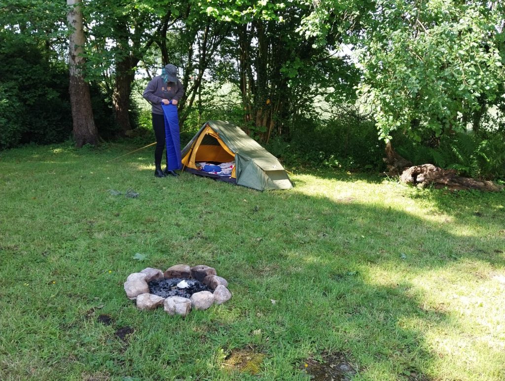 My sister stands in the garden unrolling her bed mat in front of her new tent.