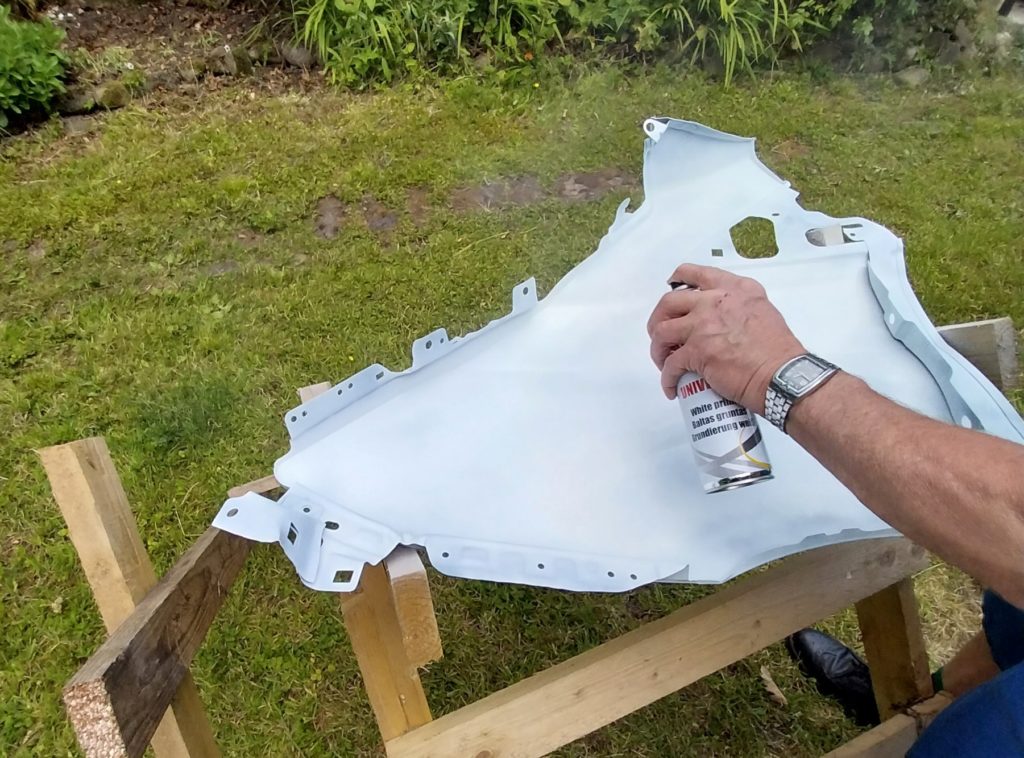 A panel balanced on a wood chopping easel, being sprayed white.